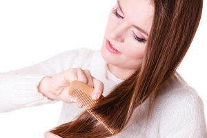 Woman combing with brush and pulls at her long hair. Being patient for nice look in daily activity.