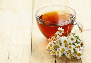 glass cup with tea and chamomile on a wooden background